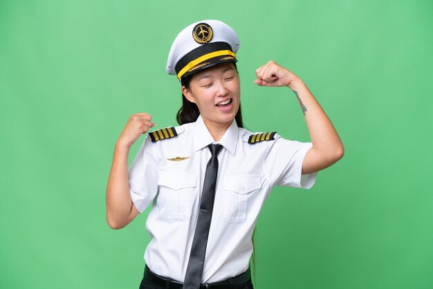 Asiatische Frau des Flugzeugpiloten vor isoliertem Hintergrund, die einen Sieg feiert