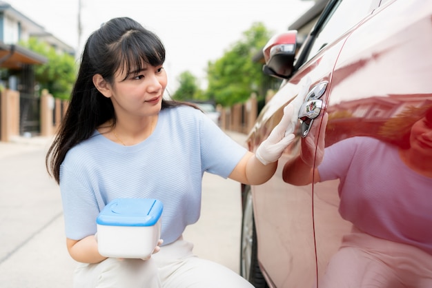 Asiatische Frau desinfiziert Türgriff des roten Autos durch Desinfektionsmittel-Einweg-Tücher aus der Schachtel. Verhindern Sie das Virus und die Bakterien, Verhindern Sie covid19, Corona-Virus