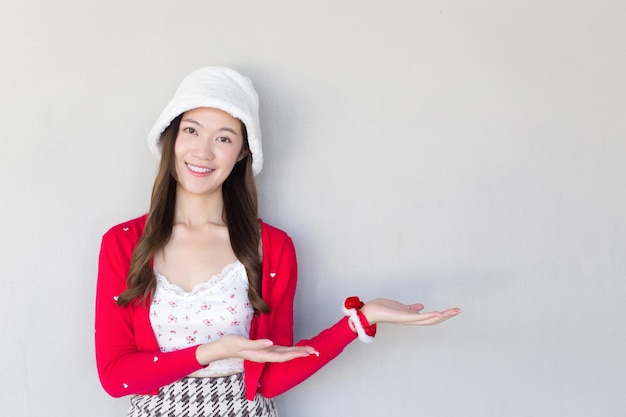 Asiatische Frau, die als Santy-Mädchen roten Mantel und weißen Hut trägt, agiert mit der Hand, um etwas zu präsentieren