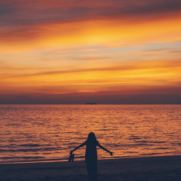 Asiatische Frau, die am Morgenhimmel mit Sonnenaufganghintergrund am Strand am Meer steht.