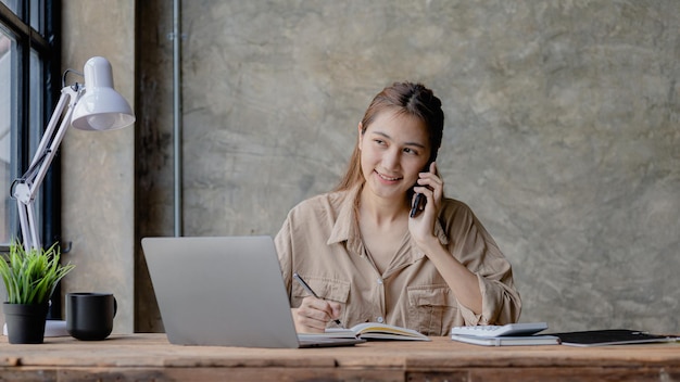 Asiatische Frau, die am Telefon spricht, ist Verkäuferin in einem Startup-Unternehmen. Sie ruft Kunden an, um Produkte und Werbeaktionen zu verkaufen. Konzept des Verkaufs von Produkten über Telefonkanäle