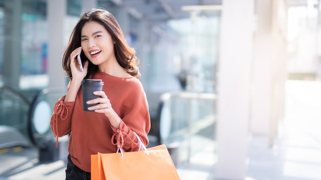 Asiatische Frau, die am Telefon spricht und Einkaufstaschen hält