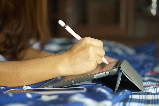 Asiatische Frau, die an einem Computer auf dem Bett arbeitet und von zu Hause aus arbeitet