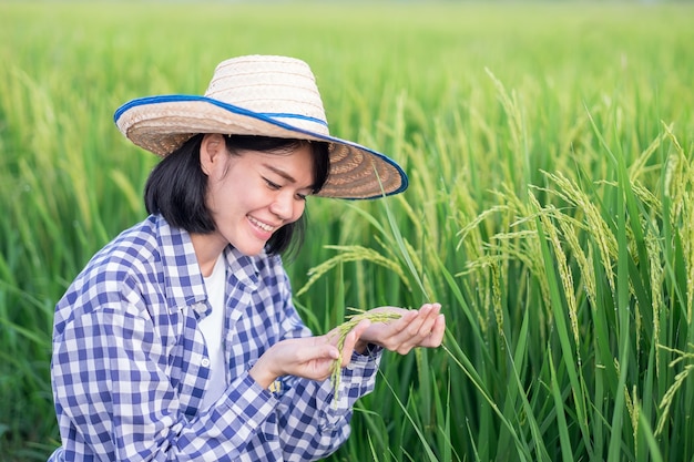 Asiatische Frau, die auf dem Gebiet sitzt und grüne Reisfelder mit einem lächelnden Gesicht hält.