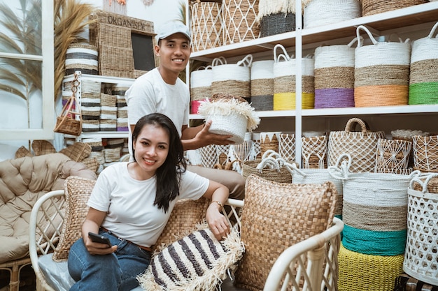 Asiatische Frau, die auf dem Sofa hält Handys und asiatischen Mann hält Korbhandwerk in der Handwerksgalerie hält