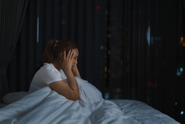 Asiatische Frau, die auf einem weißen Bett im Schlafzimmer liegt und besorgt aussieht oder mitten in der Nacht zu Hause über etwas über ihr Leben oder ihre Arbeit nachdenkt.