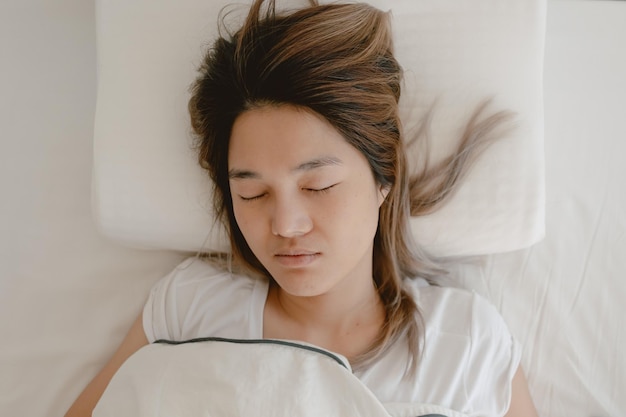 Asiatische Frau, die auf einem weißen Bett schläft, schläft und ruht sich bis zum Morgen aus