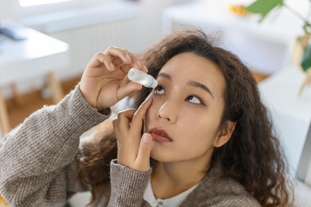 Asiatische Frau, die Augentropfen verwendet, die Augenschmiermittel fallen lassen, um trockene Augen oder an Allergien erkrankte Frauen zu behandeln, die Reizungen oder Entzündungen des Augapfels behandeln
