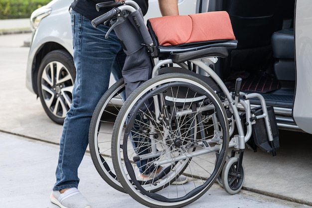 Asiatische Frau, die den Rollstuhl in ihr Auto faltet und hochhebt Barrierefreiheitskonzept