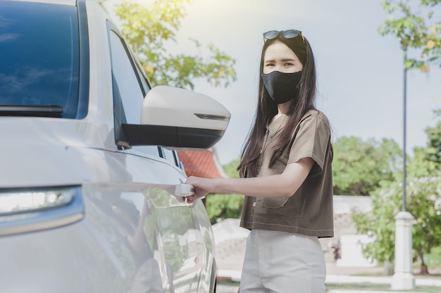 Asiatische Frau, die ein Auto mit einer medizinischen Maske betritt