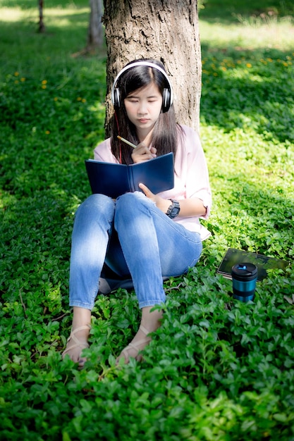 Asiatische Frau, die ein Buch liest und im Park lächeltZufriedene asiatische Frau, die ein Buch in einem Park liest