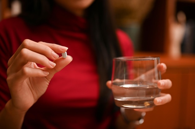 Asiatische Frau, die ein Glas Wasser und eine Vitamin- oder Medizintablette hält. beschnittenes und Nahaufnahmebild