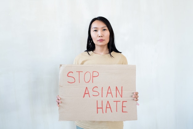 Asiatische Frau, die ein Schild hält, das Protest gegen nationale Diskriminierung ankündigt