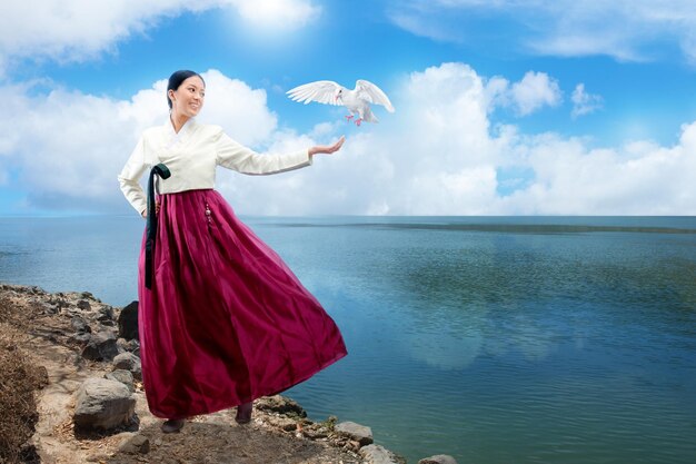 Foto asiatische frau, die ein traditionelles koreanisches nationalkostüm hanbok trägt, das mit offenen handflächen steht und fliegenden vogel zeigt