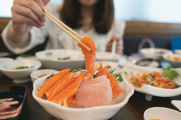 Asiatische Frau, die einen Sashimi-Lachs isst Frau mit Stäbchen, um rohen Fisch-Sashimi aus weißer Schüssel zu pflücken Frau mit Stäbchen in Scheiben geschnittenen rohen Lachs Japanisches Essen in einem japanischen Restaurant