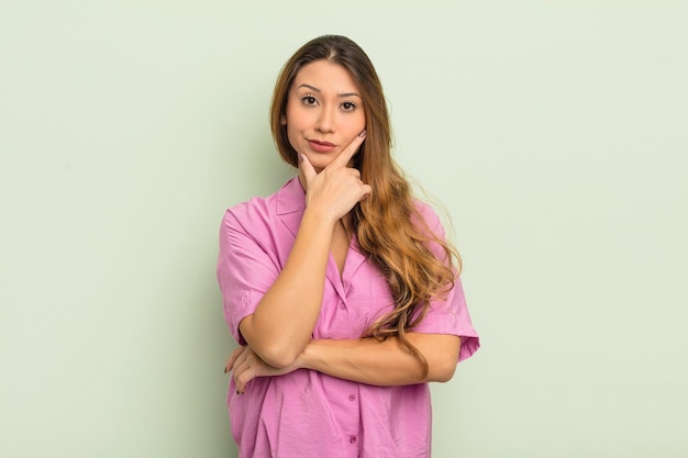 Asiatische Frau, die ernsthaft nachdenklich und misstrauisch aussieht, mit einem gekreuzten Arm und Hand auf Kinngewichtsoptionen