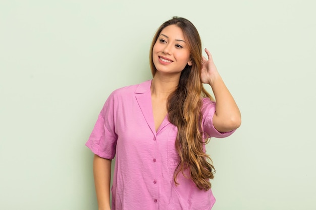 Asiatische Frau, die fröhlich und beiläufig lächelt und mit einem positiven, glücklichen und selbstbewussten Blick Hand an Kopf nimmt