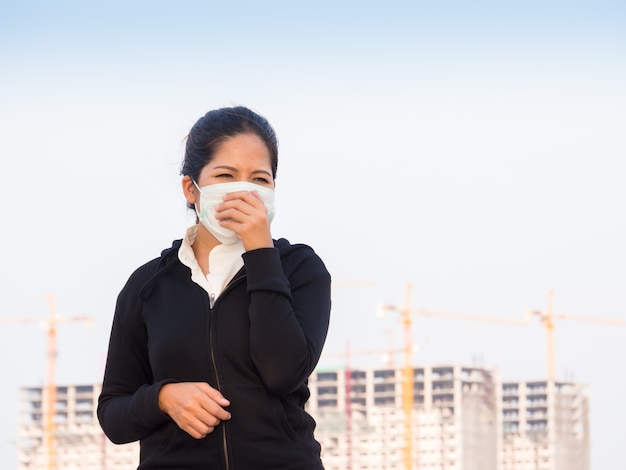 Asiatische Frau, die Gesichtsmaske trägt und durch Umweltverschmutzung hustet