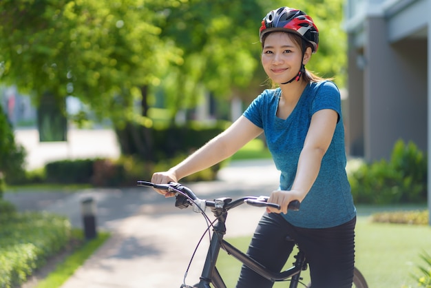 Asiatische Frau, die glücklich aussieht, während sie mit dem Fahrrad durch ihre Nachbarschaft fährt, für die tägliche Gesundheit und das Wohlbefinden, sowohl körperlich als auch geistig.