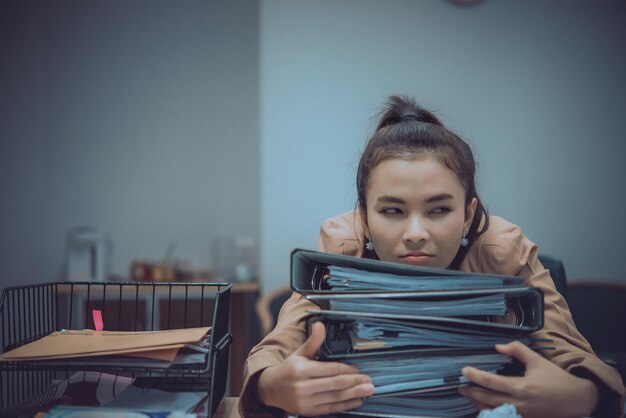 Asiatische Frau, die im Büro arbeitet, junge Geschäftsfrau, die durch Arbeitsüberlastung mit einer Menge Akte auf dem Schreibtisch gestresst ist