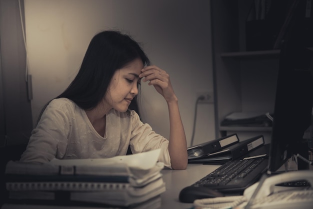 Asiatische Frau, die im Büro arbeitet, junge Geschäftsfrau, gestresst von Arbeitsüberlastung mit vielen Akten auf dem Schreibtisch