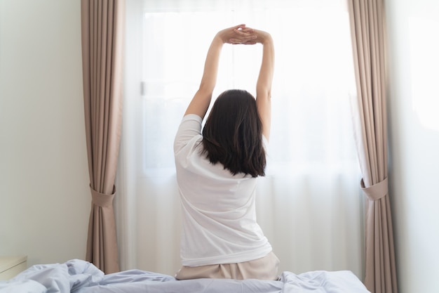 Asiatische Frau, die im Schlafzimmer nach dem Aufwachen, Rückansicht streckt