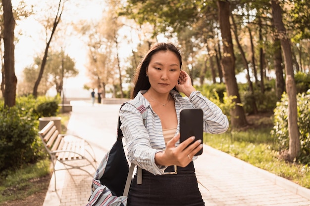 Asiatische Frau, die im Sommer im Stadtpark spaziert und Sefie am Telefon macht