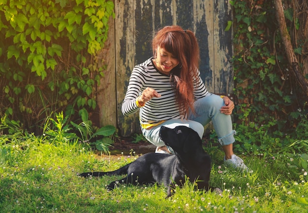 Asiatische Frau, die im Sommer mit ihrem Hund auf dem grünen Gras spielt