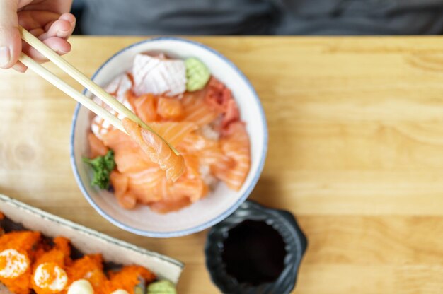 Asiatische Frau, die Lachsscheiben-Sashimi mit Reis im japanischen Restaurant isst