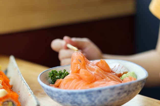 Asiatische Frau, die Lachsscheiben-Sashimi mit Reis im japanischen Restaurant isst