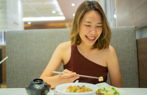 asiatische frau, die lächelt, während sie essstäbchen verwendet, um frisches essen in scheiben im restaurant zu halten