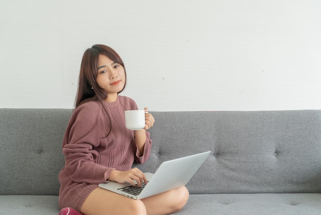 Asiatische Frau, die Laptop auf Sofa im Wohnzimmer verwendet