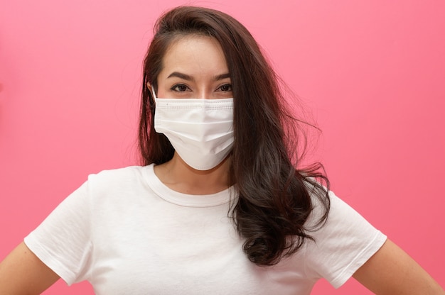 Asiatische Frau, die medizinische Gesichtsmaske auf rosa Wand trägt