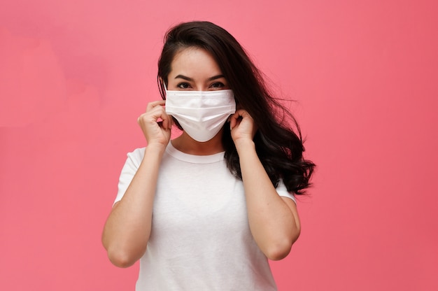 Asiatische Frau, die medizinische Gesichtsmaske auf rosa Wand trägt