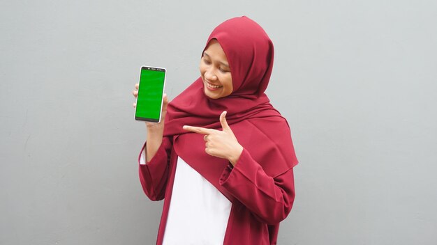 Asiatische Frau, die mit dem grünen Bildschirm auf das Handy zeigt