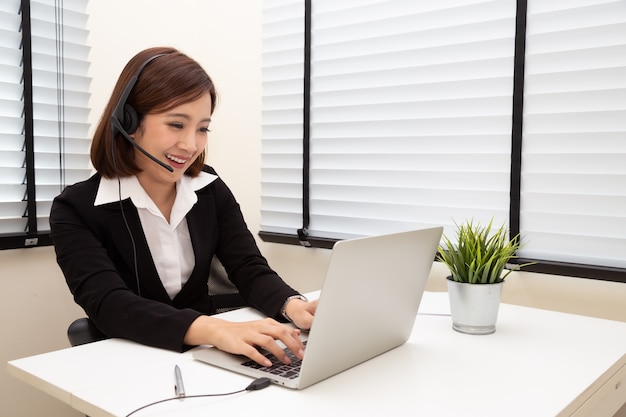 Asiatische Frau, die mit einem Headset und Laptop im Hauptschreibtisch spricht