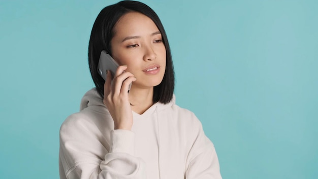 Asiatische Frau, die mit ihren Geschäftspartnern bei einem Telefonanruf spricht und ernst aussieht, isoliert auf buntem Hintergrund Gesichtsausdruck