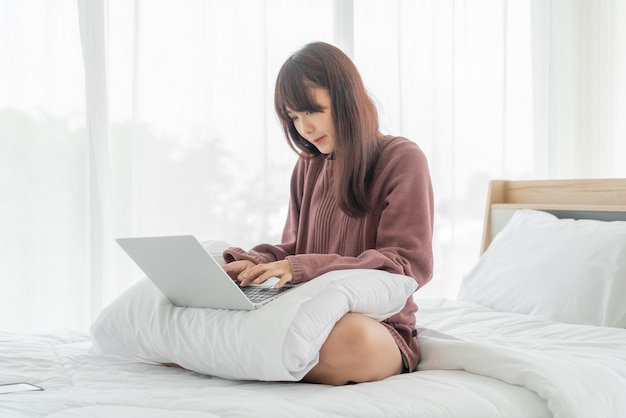 Asiatische Frau, die mit Laptop auf Bett arbeitet