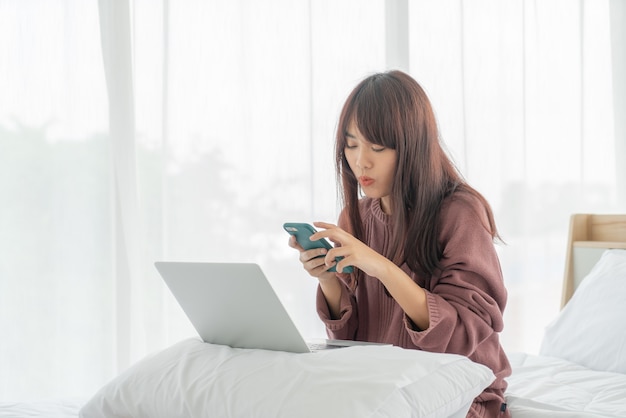 Asiatische Frau, die mit Laptop auf Bett arbeitet