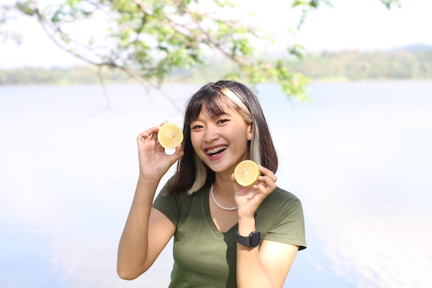 Asiatische Frau, die morgens zwei gelbe Orangen hält