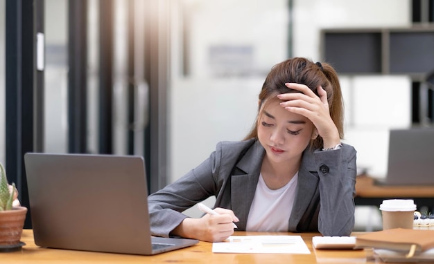 Asiatische Frau, die müde und nachdenklich ist, wenn sie im Büro mit einem Tablet arbeitet