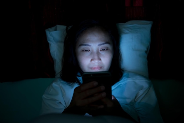 Asiatische Frau, die nachts auf dem Smartphone im Bett spieltThailänderSüchtige soziale Medien