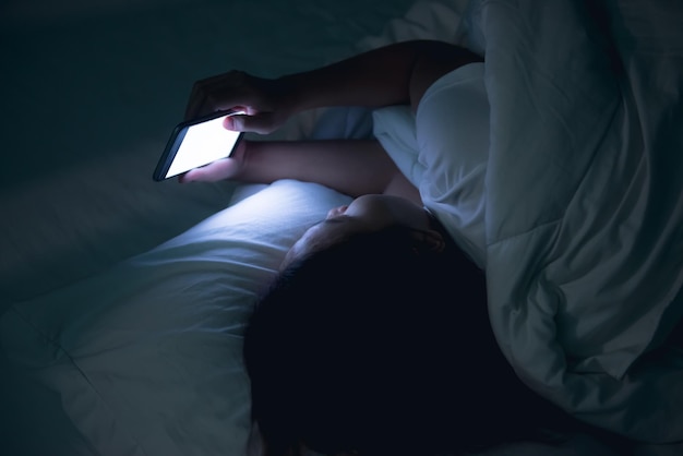 Asiatische Frau, die nachts auf dem Smartphone im Bett spieltThailänderSüchtige soziale Medien