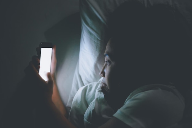 Foto asiatische frau, die nachts auf dem smartphone im bett spieltthailändersüchtige soziale medien