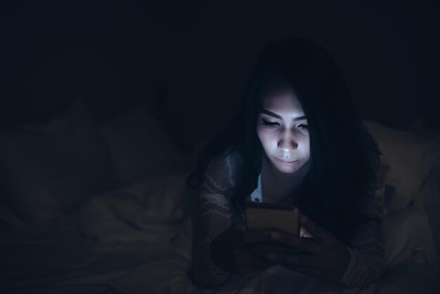 Asiatische Frau, die nachts auf dem Smartphone im Bett spieltThailänderSüchtige soziale Medien