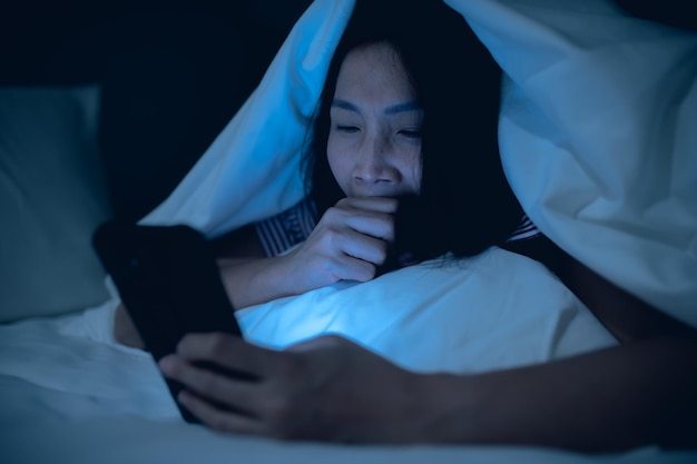 Asiatische Frau, die nachts auf dem Smartphone im Bett spieltThailänderSüchtige soziale Medien