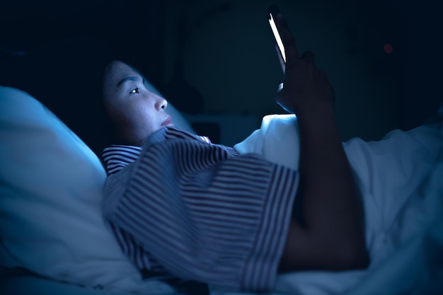 Asiatische Frau, die nachts auf dem Smartphone im Bett spieltThailänderSüchtige soziale Medien