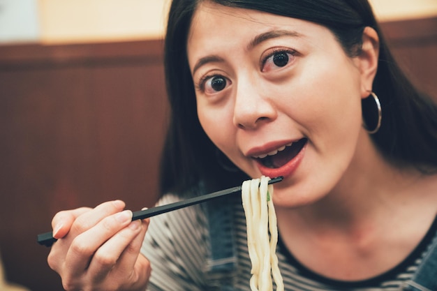 asiatische frau, die nudeln im japanischen lokalen restaurant isst. schöne Dame mit lächelndem Gesicht, während sie an einem schönen Ort sitzt und zu Mittag isst. weiblicher offener mund, der mahlzeit mit udon ramen in chinatown hat.
