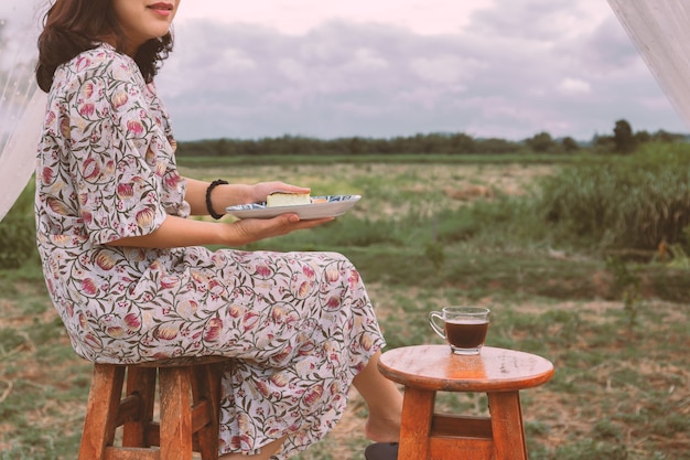 Asiatische Frau, die Platte mit Käsekuchen und Tasse Kaffee im Freien hält.