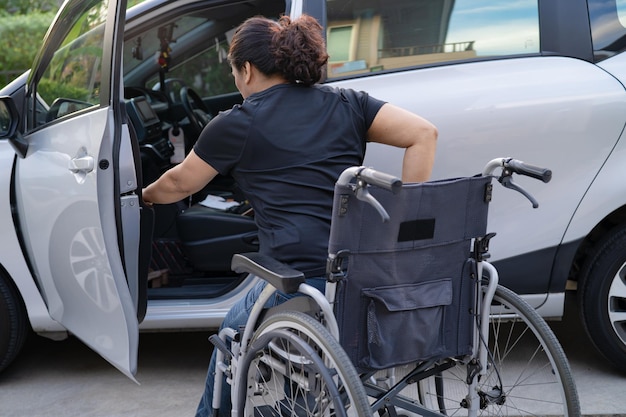 Asiatische Frau, die Rollstuhl in ihr Auto faltet und anhebt. Konzept der Barrierefreiheit.